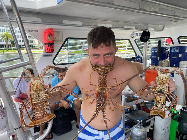 Image of a man holding Florida Spiny Lobsters in each hand and one in his mouth by the tail.